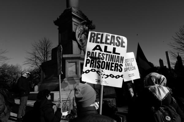 At a Palestine solidarity rally, protestors carry signs that say "RELEASE ALL PALESTINIAN PRISONERS" and "PROTECT FREE SPEECH."