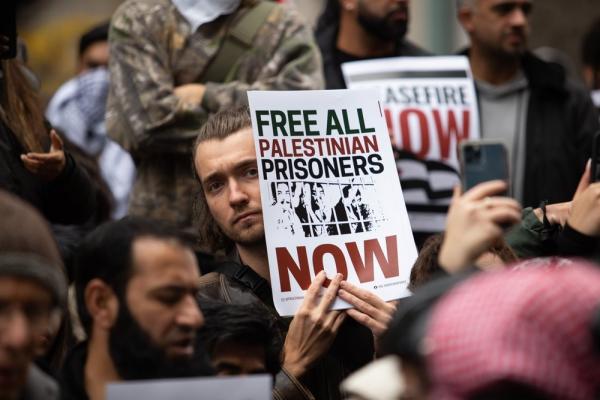 A protestor carries a sign that reads "FREE ALL PALESTINIAN PRISONERS NOW."