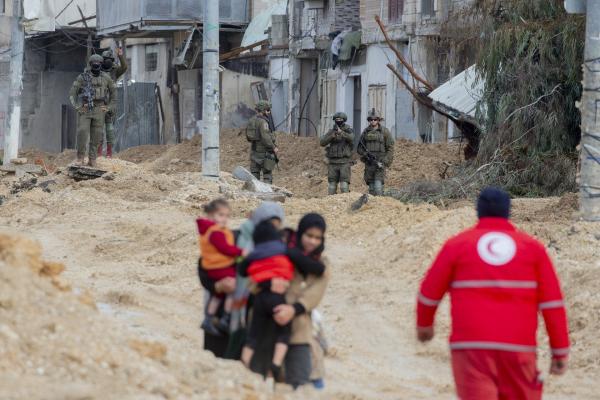 Palestinian women carry small children as they walk over rubble in the Nur Shams refugee camp as Israeli soldiers look on, in the midst of their ethnic cleansing of the camp. February 10, 2025.