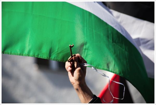 A person holds a key symbolizing the Palestinian right of return in front of a Palestinian flag.