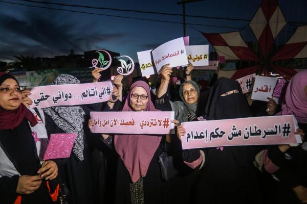 Palestinian women in Gaza hold up signs at a breast cancer awareness event. They carry Arabic-language signs that read "cancer is not a death sentence," "I am in pain, medicine is my right," "do not hesitate, your checkup is hope and safety," and "your smile is life." October 10, 2019.