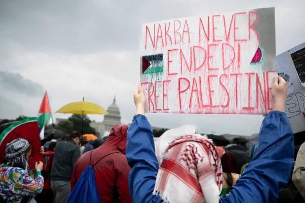 A protestor holds up a sign that says "NAKBA NEVER ENDED! FREE PALESTINE."