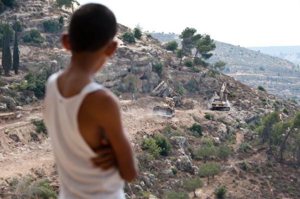 A Palestinian boy looks on the Israeli mliitary uses Caterpillar equipment to clear out Palestinian land to make way for the construction of Israel's apartheid wall near the town of al-Walaja in the occupied West Bank. September 5, 2001.